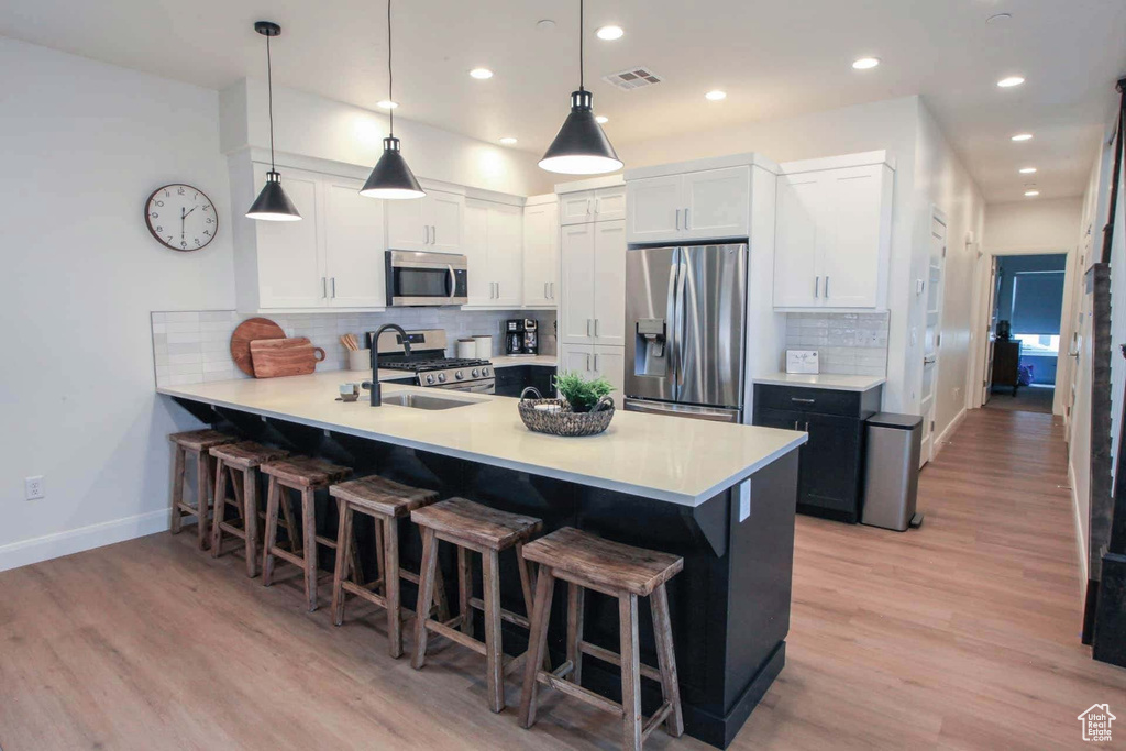 Kitchen featuring light hardwood / wood-style floors, tasteful backsplash, stainless steel appliances, pendant lighting, and white cabinets