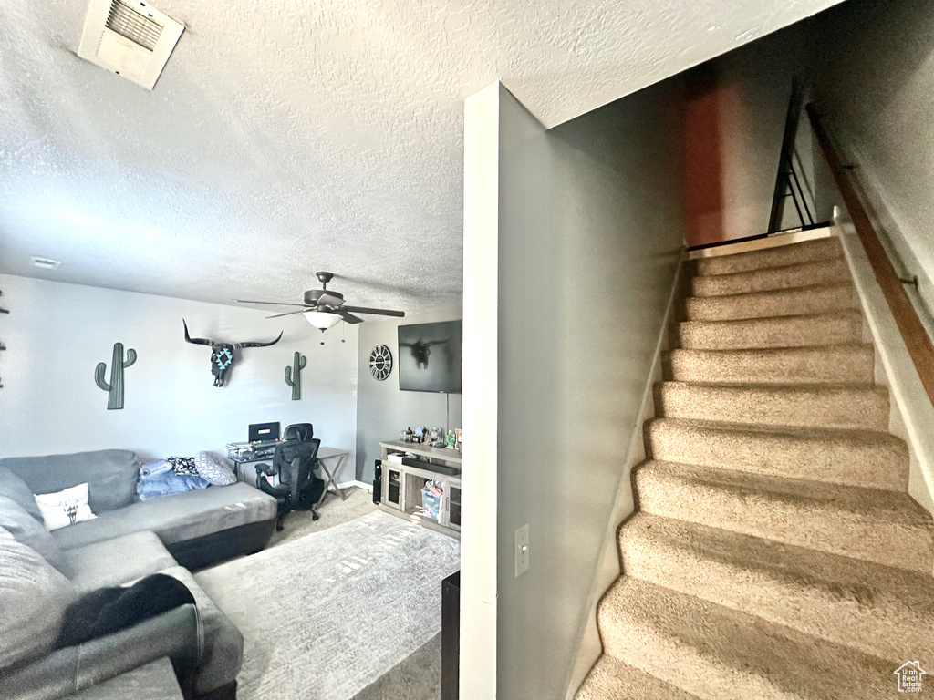 Staircase with ceiling fan, a textured ceiling, and carpet