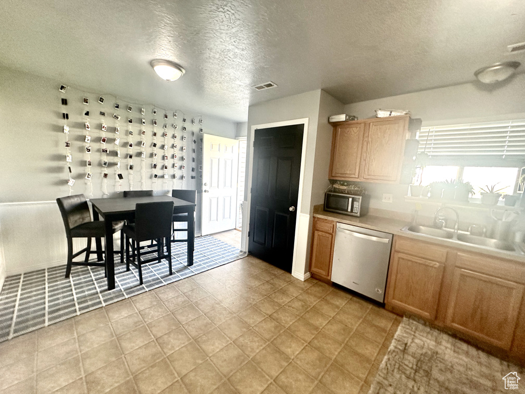 Kitchen with sink, a textured ceiling, light tile patterned floors, and stainless steel appliances