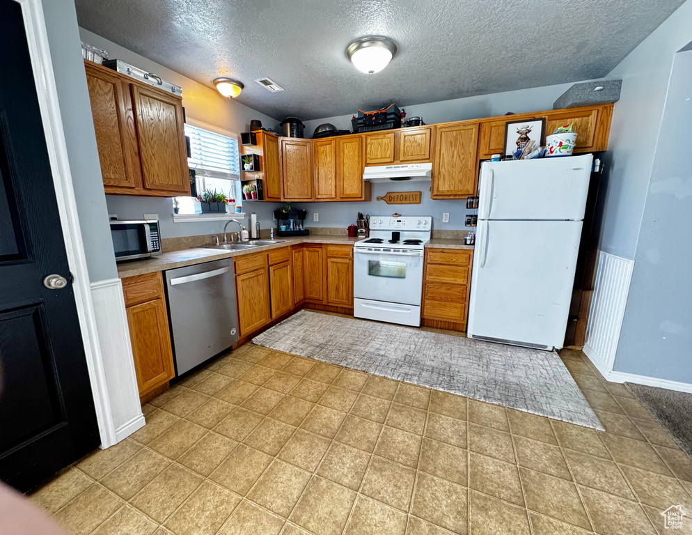Kitchen featuring a sink, light countertops, a textured ceiling, under cabinet range hood, and stainless steel appliances