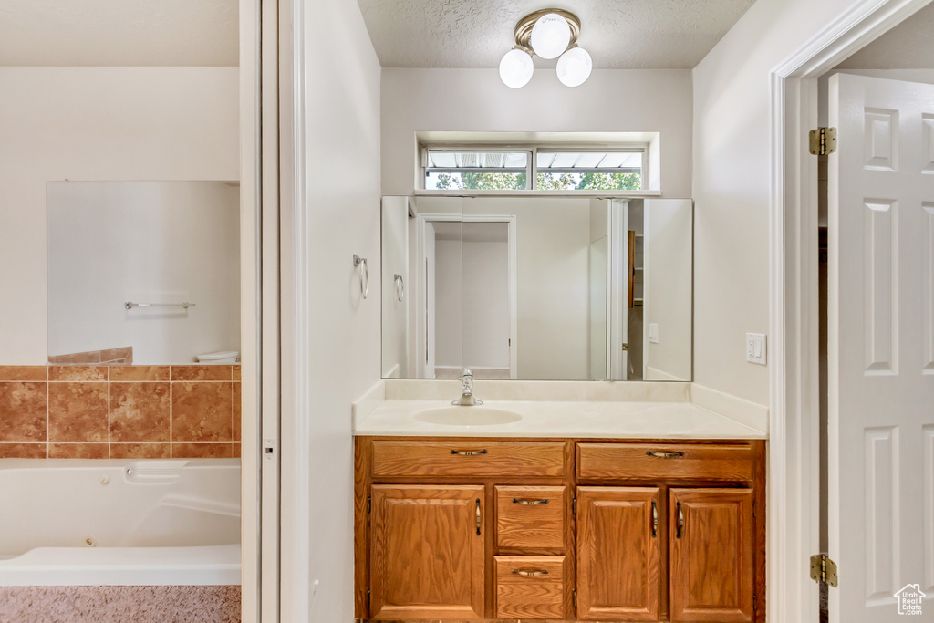 Bathroom with a textured ceiling, tiled tub, and vanity