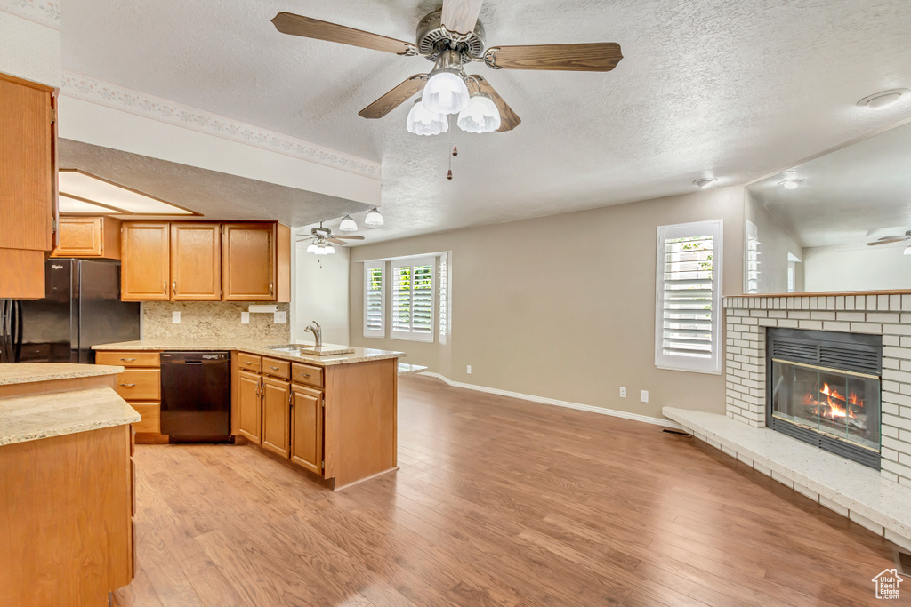 Kitchen with light wood-type flooring, lofted ceiling, a brick fireplace, and black appliances