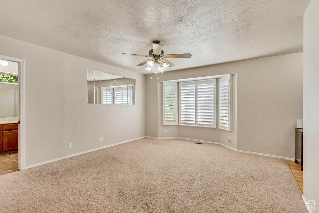 Unfurnished room with ceiling fan, light carpet, a textured ceiling, and a healthy amount of sunlight