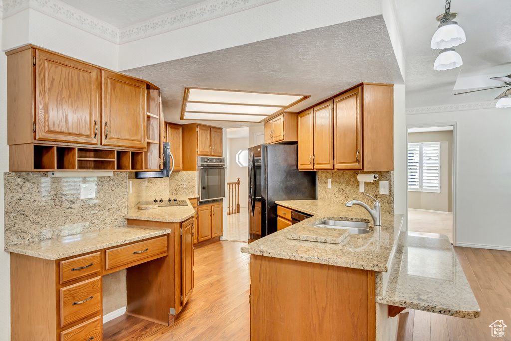 Kitchen with backsplash, light hardwood / wood-style flooring, light stone counters, and black appliances