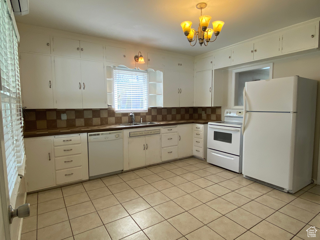 Kitchen featuring decorative backsplash, a chandelier, sink, light tile patterned floors, and white appliances