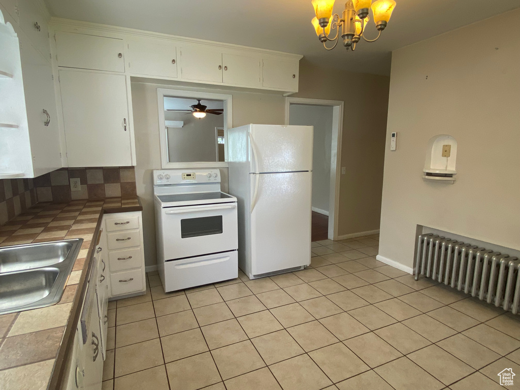 Kitchen featuring white appliances, ceiling fan with notable chandelier, tasteful backsplash, tile countertops, and white cabinetry