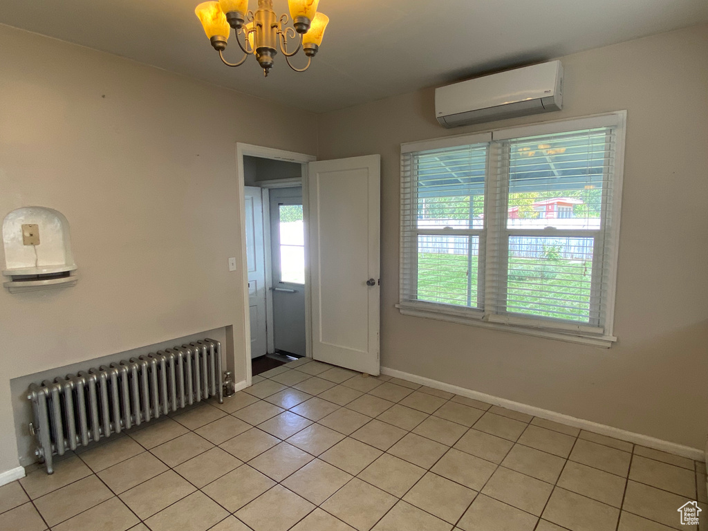 Empty room featuring light tile patterned floors, a wall mounted air conditioner, a notable chandelier, and radiator