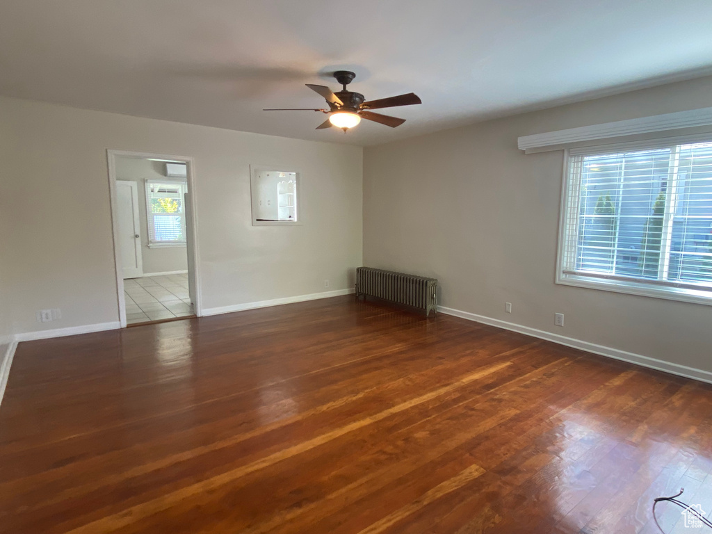 Empty room featuring radiator heating unit, dark hardwood / wood-style flooring, ceiling fan, and a wealth of natural light