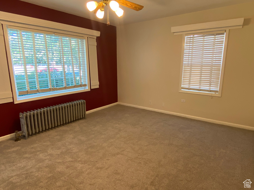 Spare room featuring carpet floors, a healthy amount of sunlight, radiator, and ceiling fan