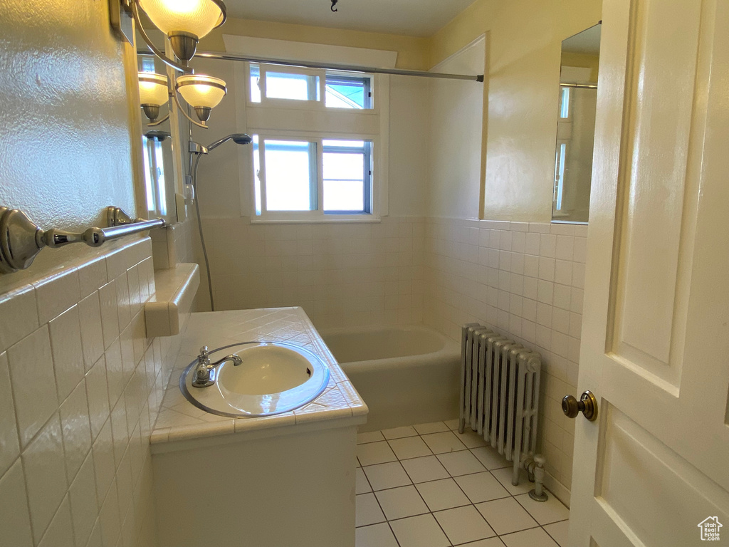 Bathroom featuring bathtub / shower combination, tile walls, tile patterned floors, radiator heating unit, and vanity