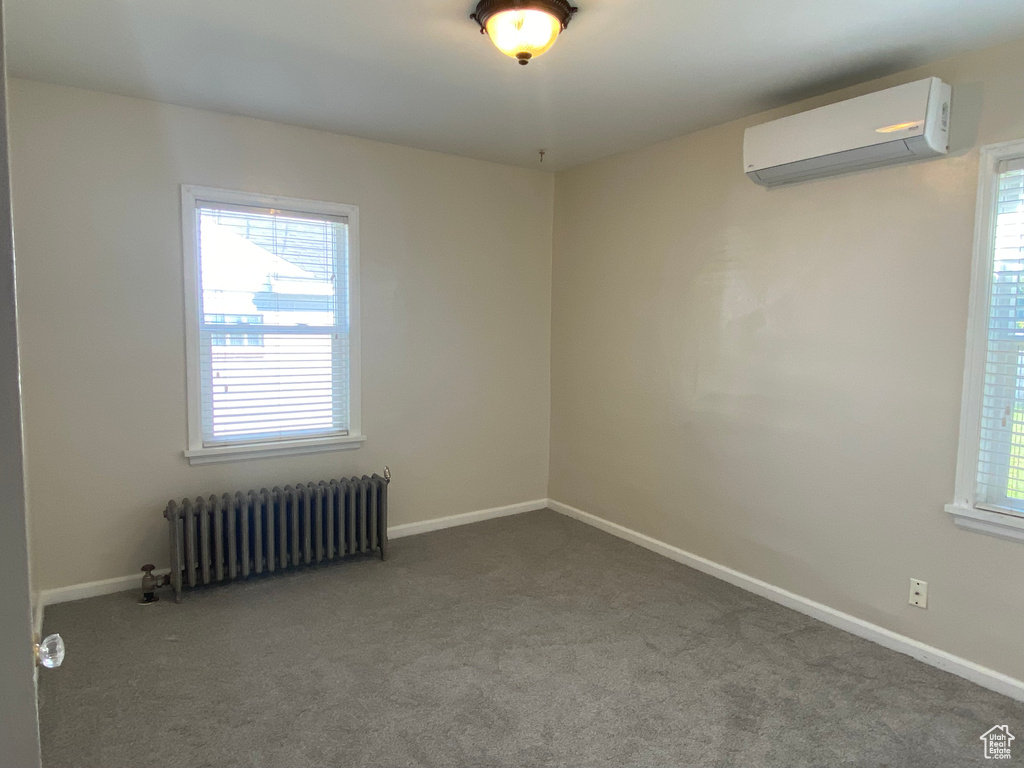 Unfurnished room featuring carpet floors, radiator heating unit, and a wall unit AC