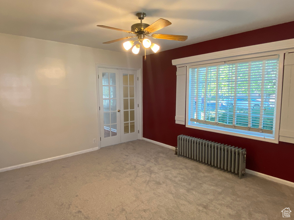 Empty room featuring light carpet, radiator, ceiling fan, and french doors