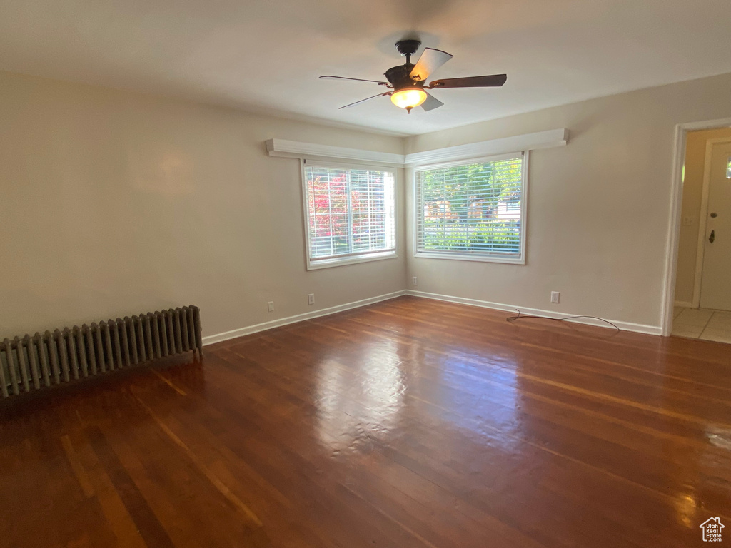 Empty room featuring radiator heating unit, ceiling fan, and dark hardwood / wood-style flooring