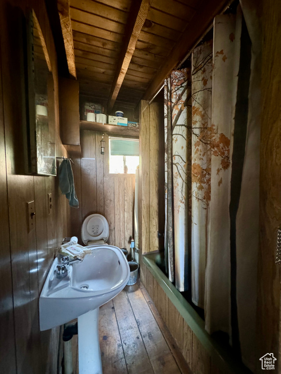 Bathroom with wood walls, shower / bath combo, wooden ceiling, hardwood / wood-style flooring, and beamed ceiling