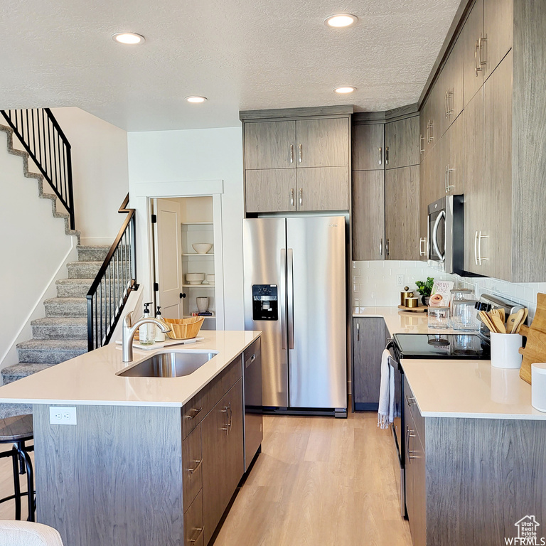 Kitchen with light hardwood / wood-style floors, sink, stainless steel appliances, and a kitchen island with sink