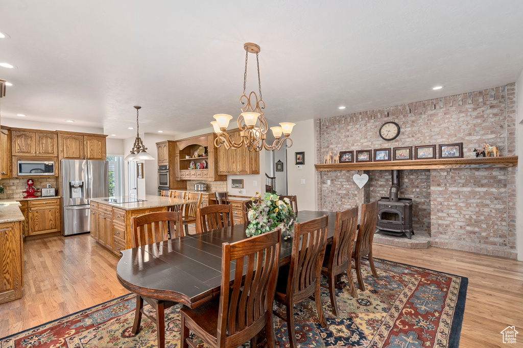 Dining room with an inviting chandelier, light hardwood / wood-style floors, brick wall, and a wood stove