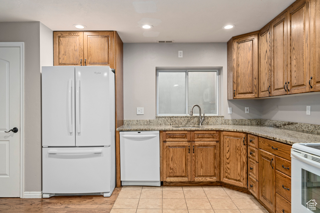 Kitchen featuring light stone countertops, sink, light tile patterned floors, and white appliances