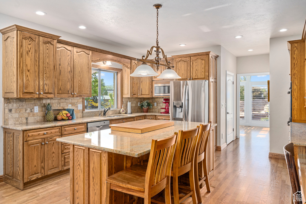 Kitchen with backsplash, hanging light fixtures, light hardwood / wood-style flooring, a kitchen island, and stainless steel appliances