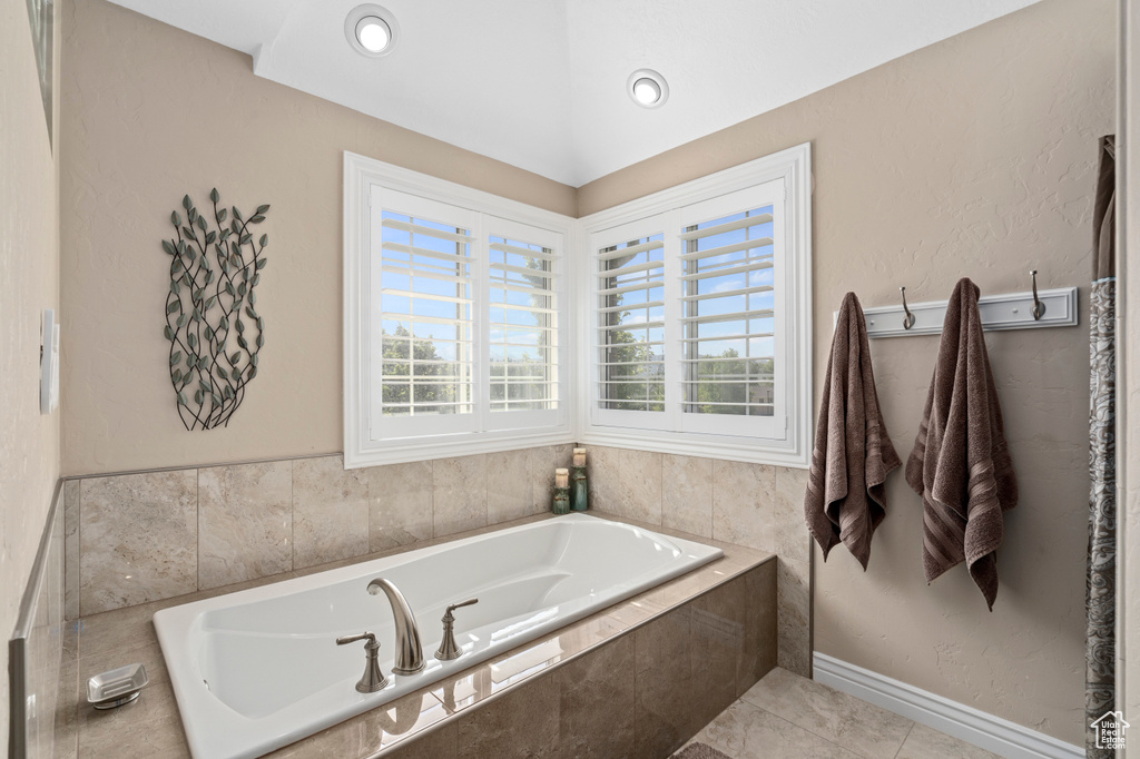 Bathroom with a relaxing tiled tub, plenty of natural light, and tile patterned floors