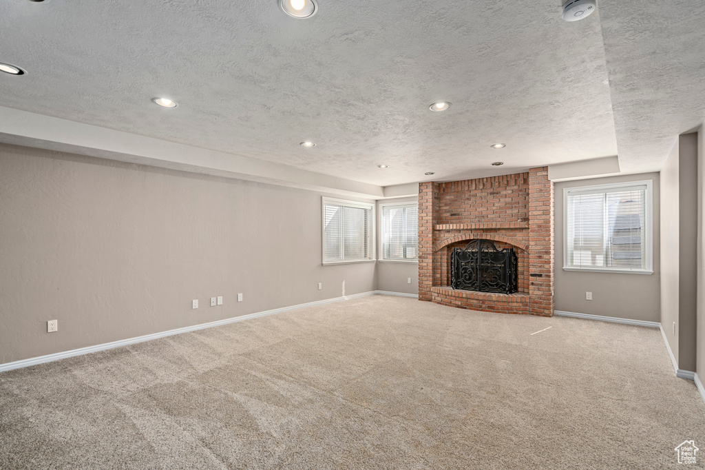 Unfurnished living room with light colored carpet, a fireplace, a textured ceiling, and brick wall