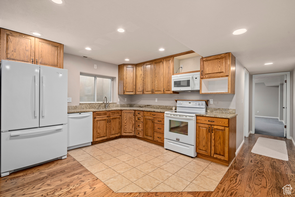 Kitchen with sink, light hardwood / wood-style flooring, light stone counters, and white appliances