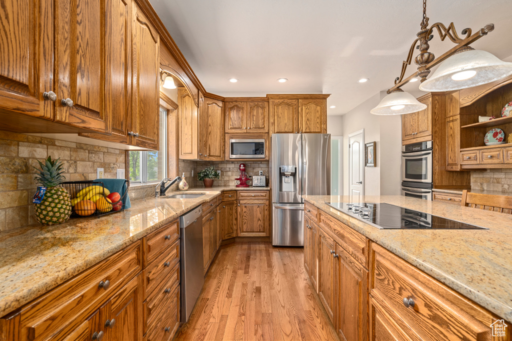 Kitchen with backsplash, stainless steel appliances, light hardwood / wood-style floors, sink, and light stone countertops