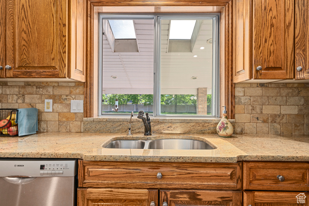 Kitchen with backsplash, dishwasher, a skylight, sink, and light stone countertops