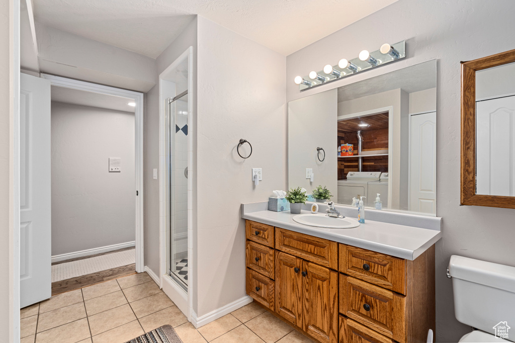 Bathroom featuring an enclosed shower, tile patterned floors, vanity, toilet, and independent washer and dryer