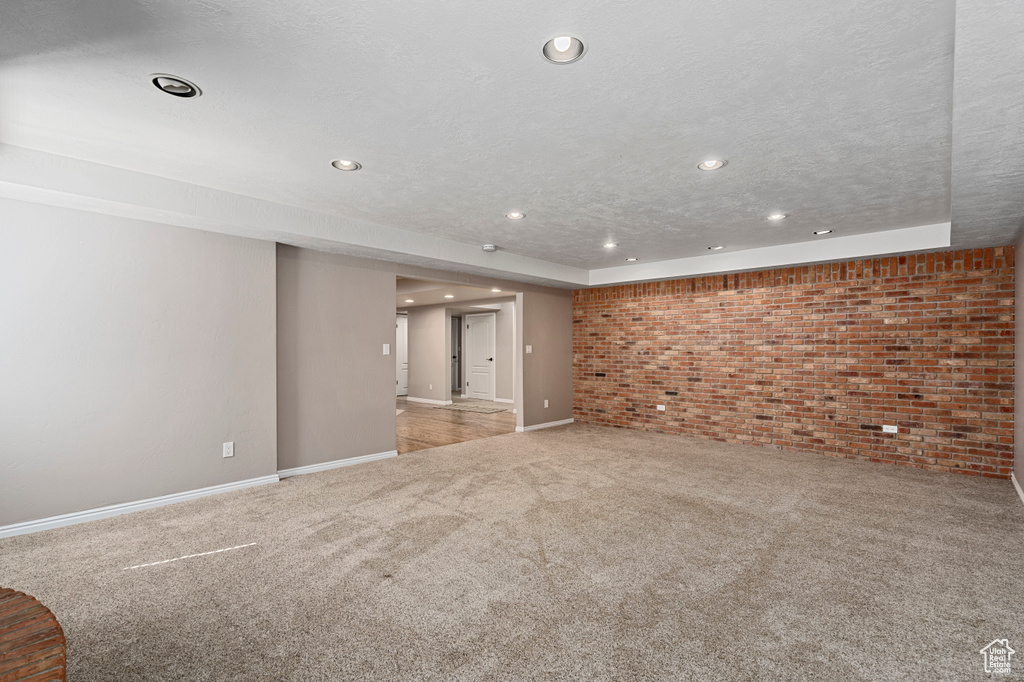 Carpeted spare room with a textured ceiling and brick wall