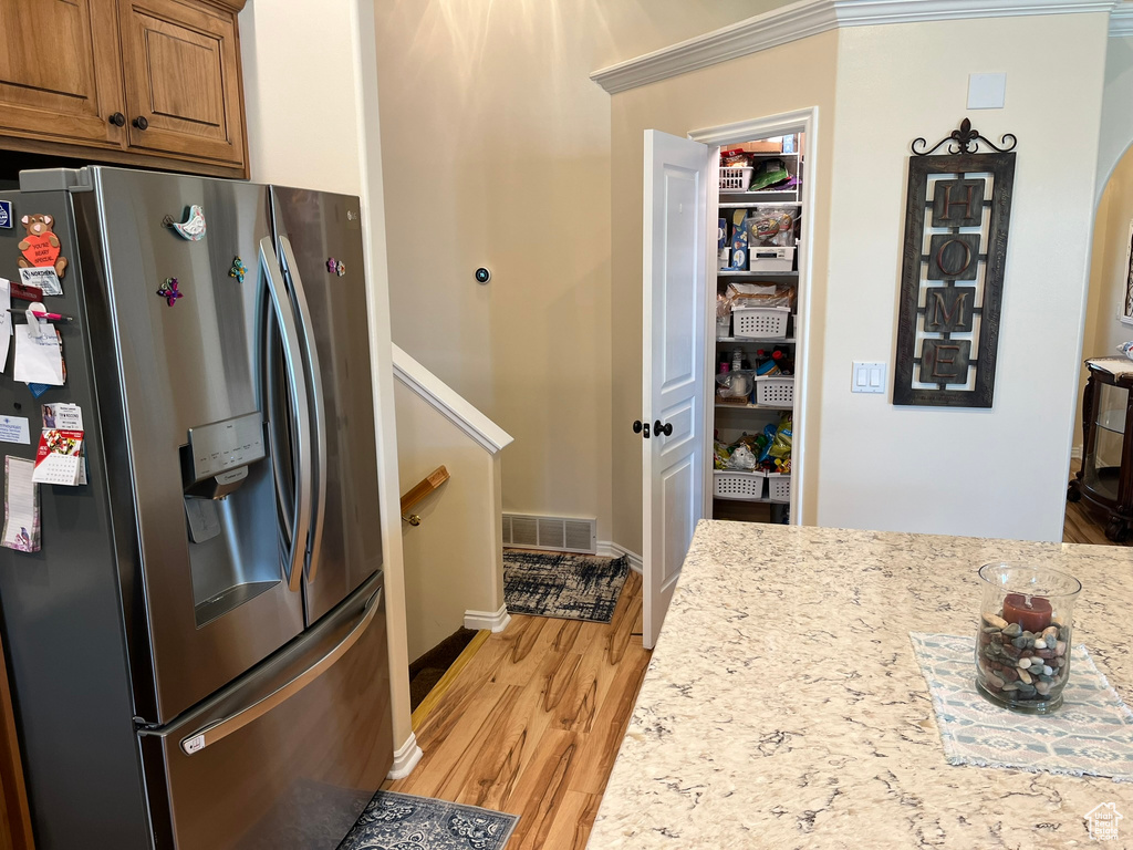 Kitchen featuring stainless steel fridge, light hardwood / wood-style floors, ornamental molding, and light stone counters