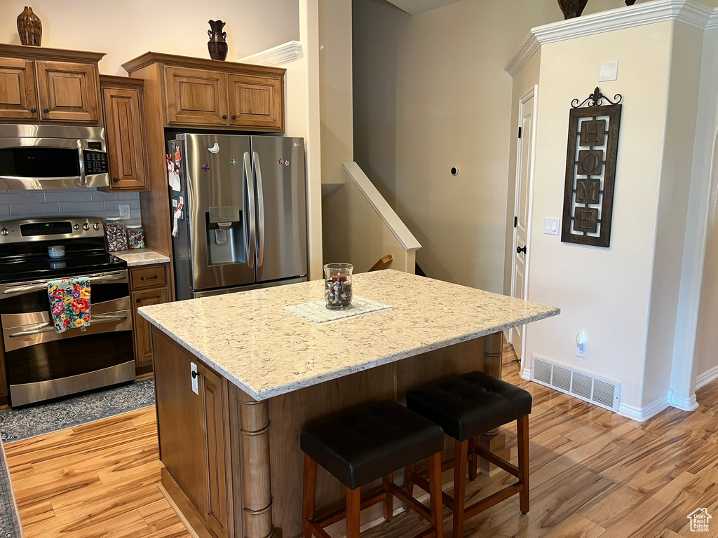 Kitchen with decorative backsplash, a center island, light wood-type flooring, and stainless steel appliances