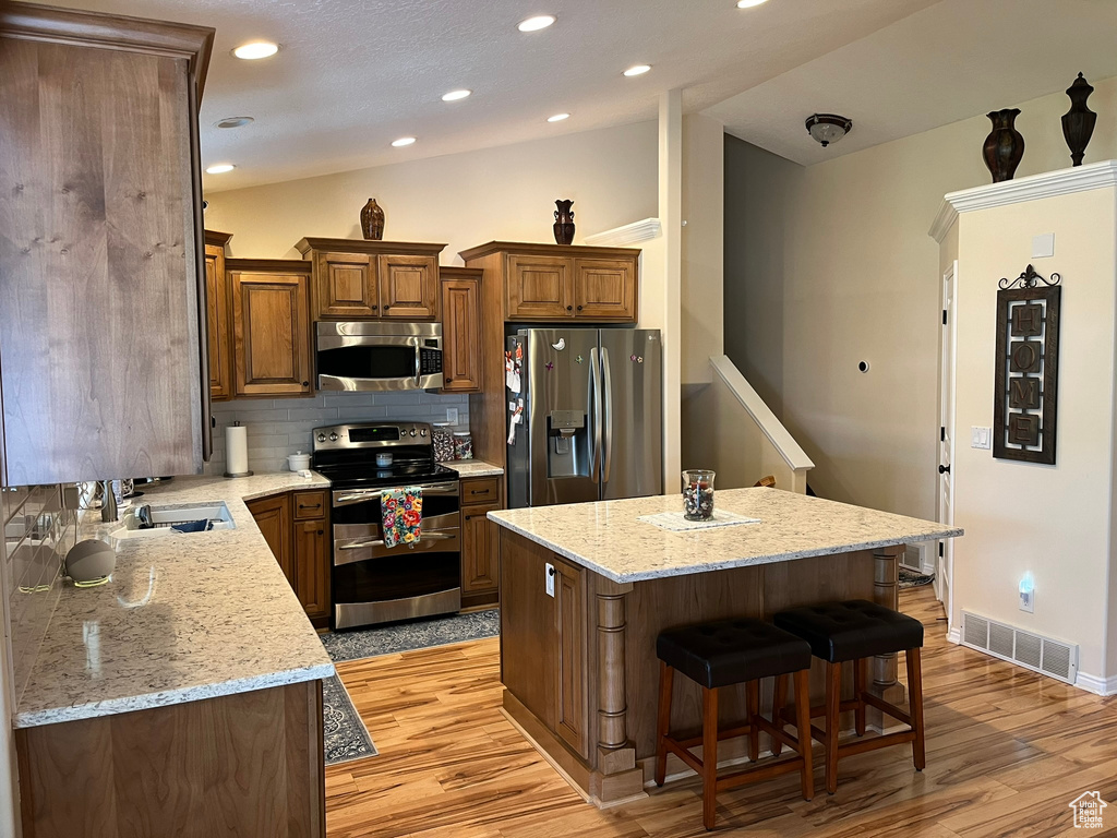 Kitchen with stainless steel appliances, tasteful backsplash, sink, light wood-type flooring, and a kitchen island