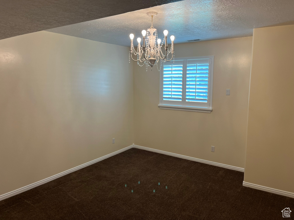 Empty room featuring a textured ceiling, carpet floors, and a chandelier