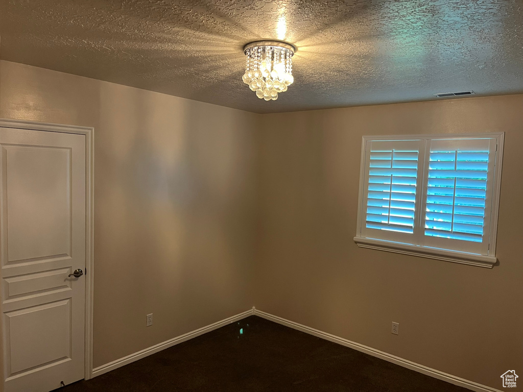 Carpeted spare room featuring a textured ceiling and a notable chandelier