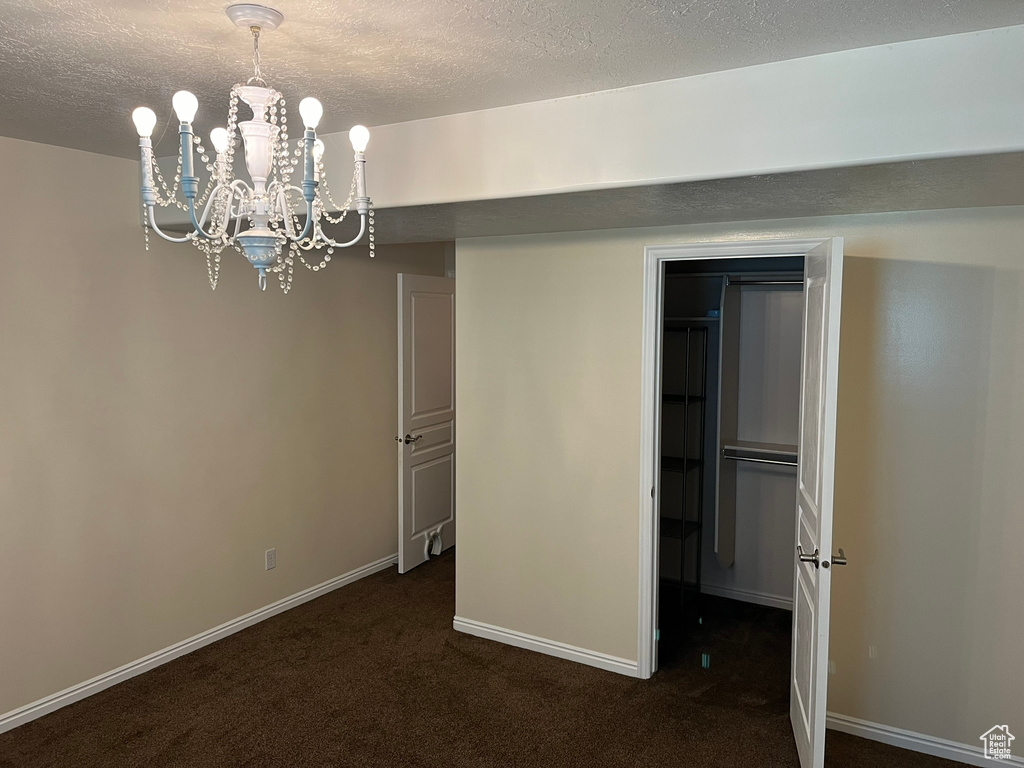 Unfurnished bedroom with a notable chandelier, a closet, a textured ceiling, and dark colored carpet