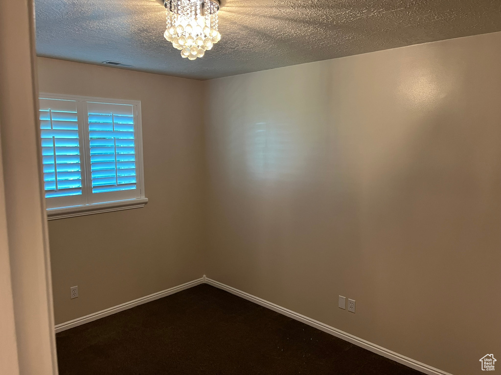 Unfurnished room with an inviting chandelier, a textured ceiling, and carpet floors