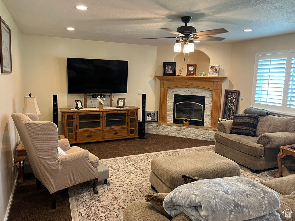 Carpeted living room with ceiling fan, a stone fireplace, and a textured ceiling