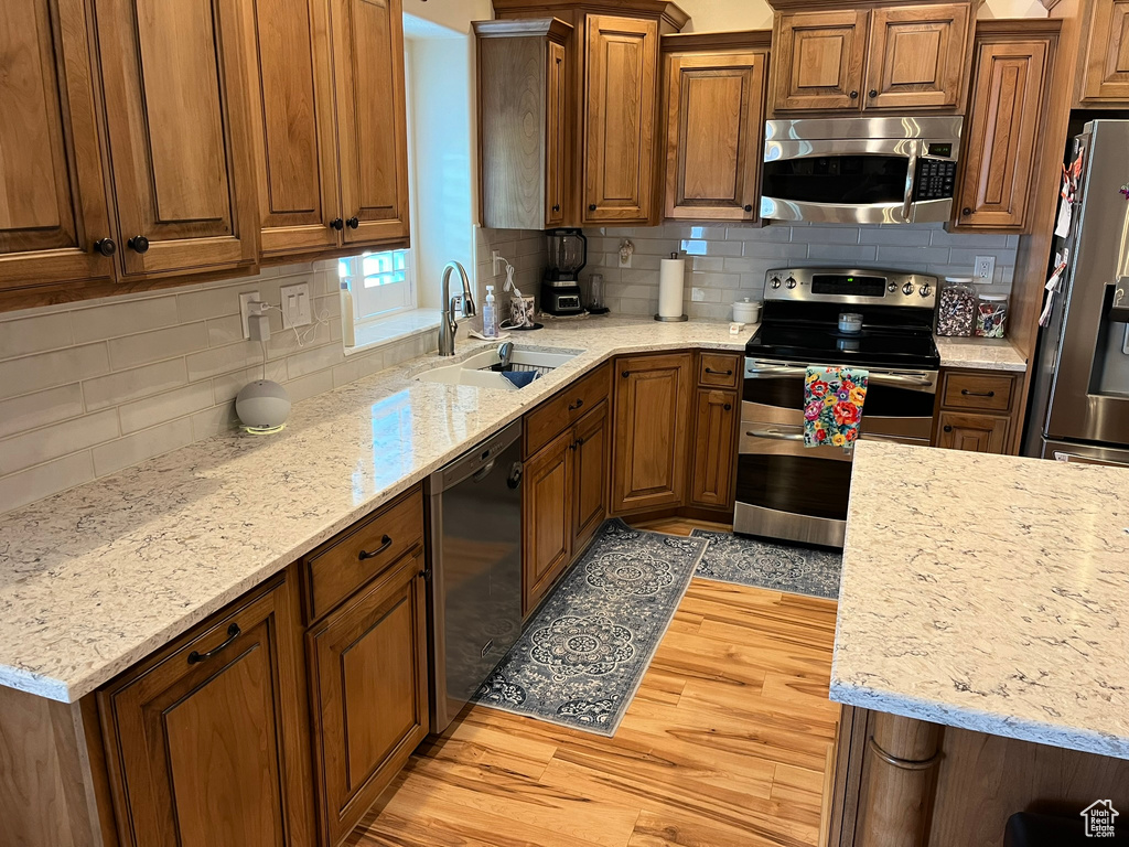 Kitchen with backsplash, sink, light wood-type flooring, light stone countertops, and stainless steel appliances