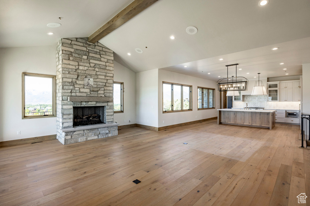 Unfurnished living room with a wealth of natural light, beam ceiling, light hardwood / wood-style floors, and a fireplace