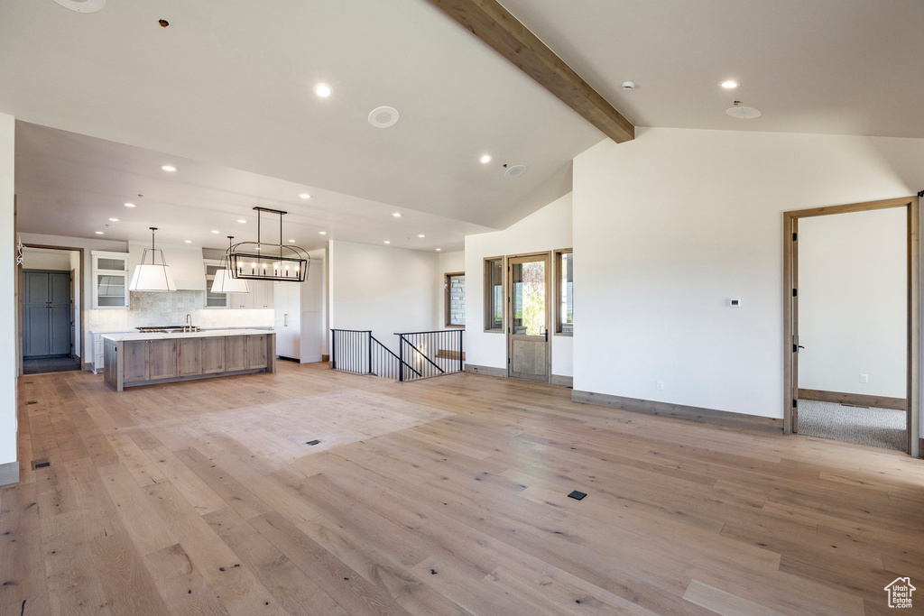 Unfurnished living room featuring sink, beam ceiling, light hardwood / wood-style floors, and high vaulted ceiling