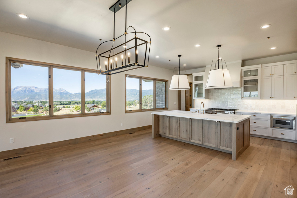 Kitchen featuring a mountain view, an island with sink, light wood-type flooring, and tasteful backsplash