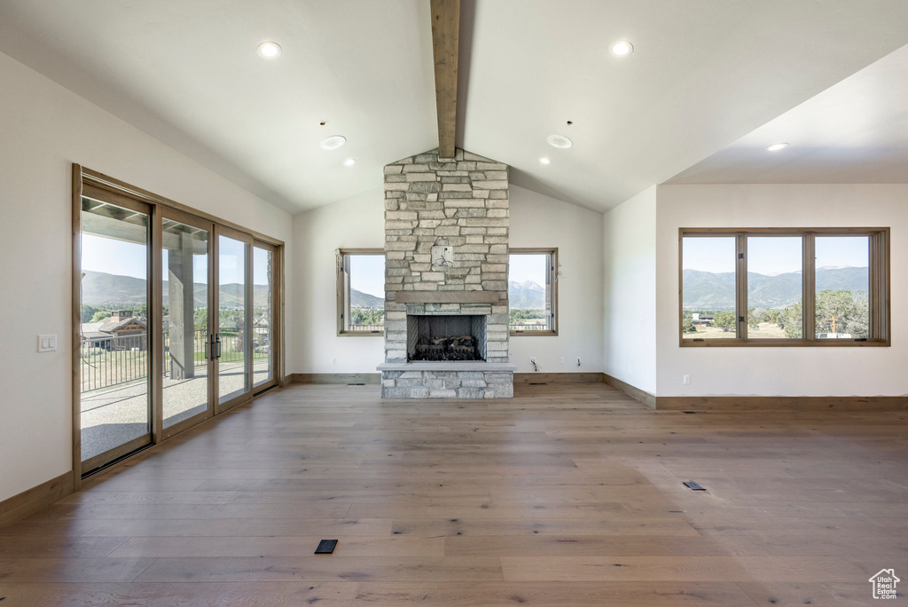 Unfurnished living room with beam ceiling, hardwood / wood-style flooring, a fireplace, and a healthy amount of sunlight