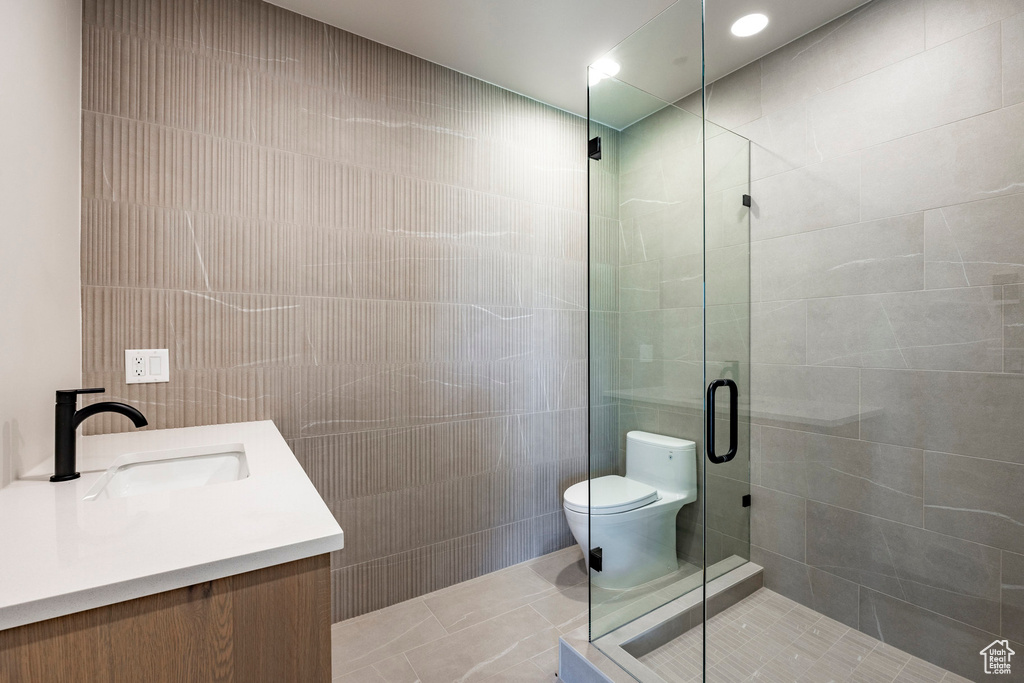 Bathroom with tile walls, an enclosed shower, tile patterned flooring, vanity, and toilet