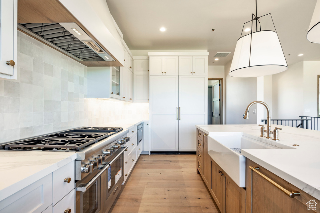 Kitchen with light hardwood / wood-style flooring, backsplash, pendant lighting, range with two ovens, and white cabinetry