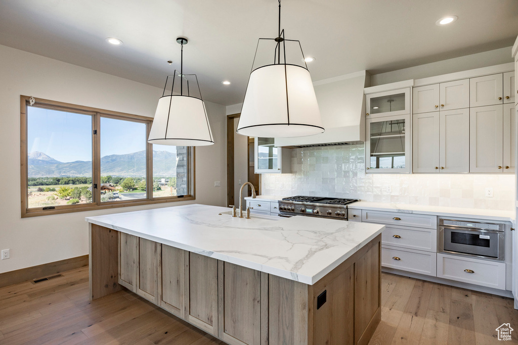 Kitchen with tasteful backsplash, white cabinetry, light hardwood / wood-style flooring, and a kitchen island with sink