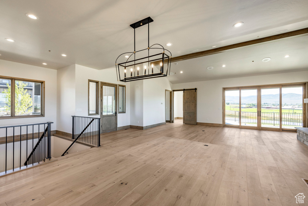 Spare room with light wood-type flooring, a healthy amount of sunlight, and a chandelier