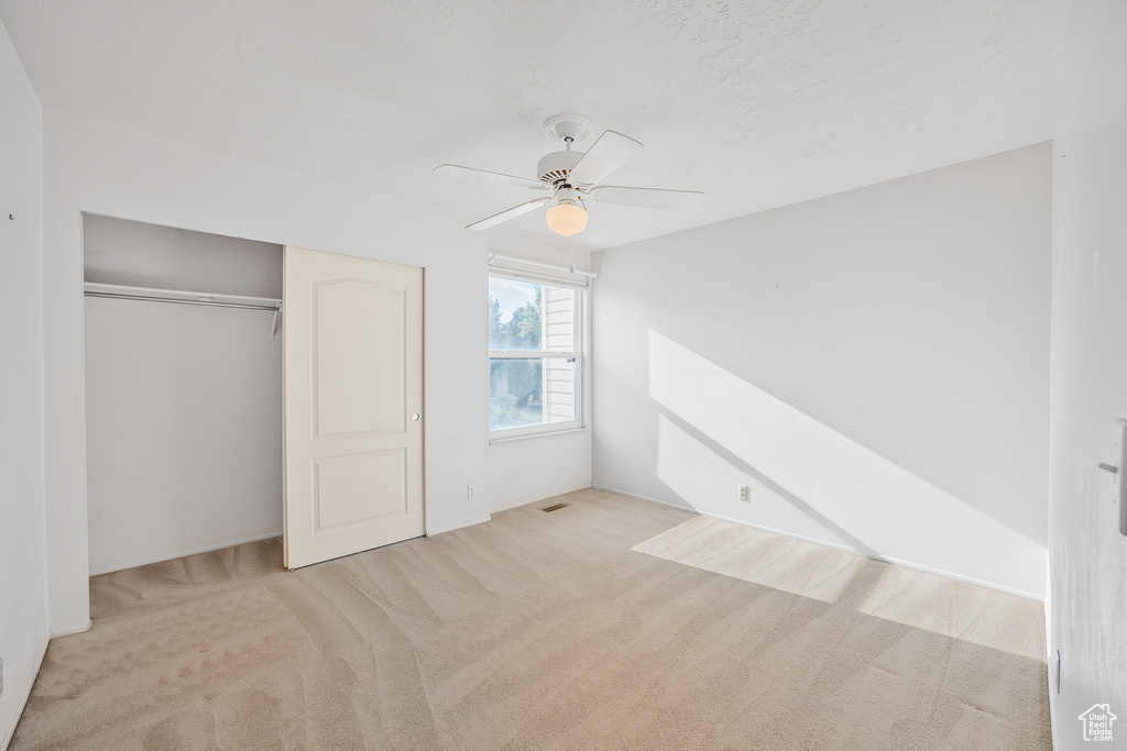 Unfurnished bedroom featuring ceiling fan, light carpet, and a closet