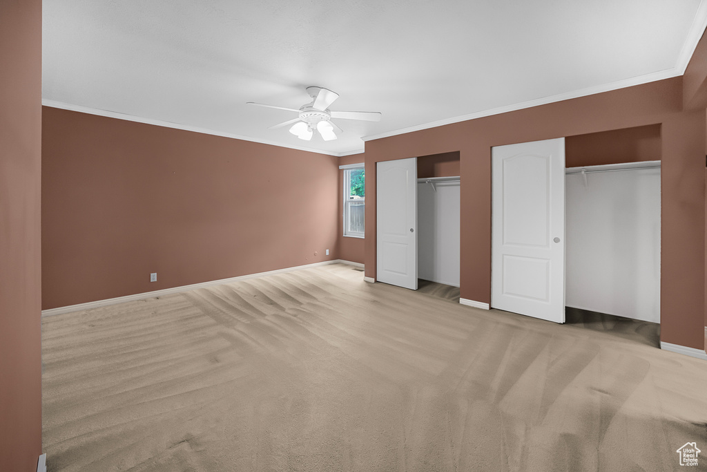 Unfurnished bedroom with ceiling fan, multiple closets, crown molding, and light colored carpet