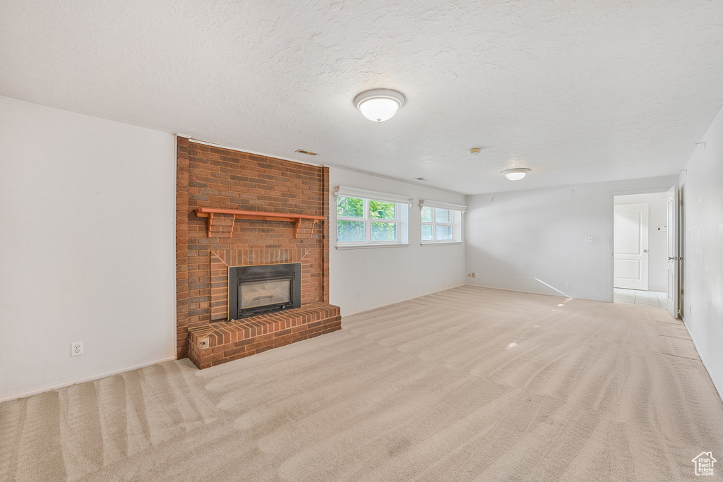 Unfurnished living room with a textured ceiling, light carpet, and a fireplace