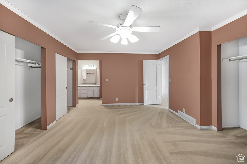 Unfurnished bedroom featuring ornamental molding, two closets, ceiling fan, connected bathroom, and light carpet